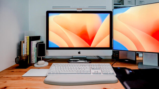 木製の机にMacデスクトップコンピューターとデュアルディスプレイが設置された作業スペース